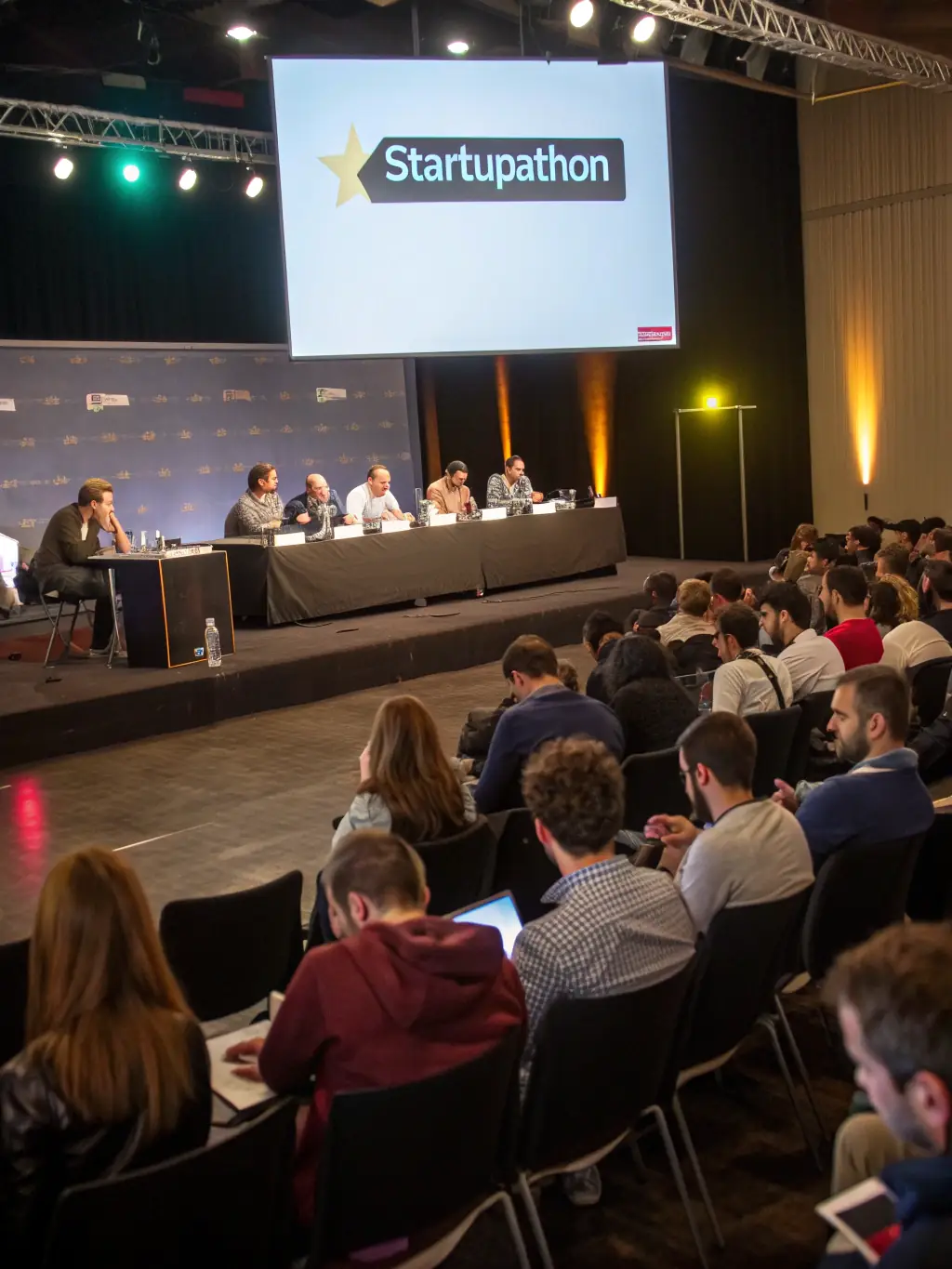 A photograph of a startup pitch competition at a conference in Delhi, India, with judges and audience members.